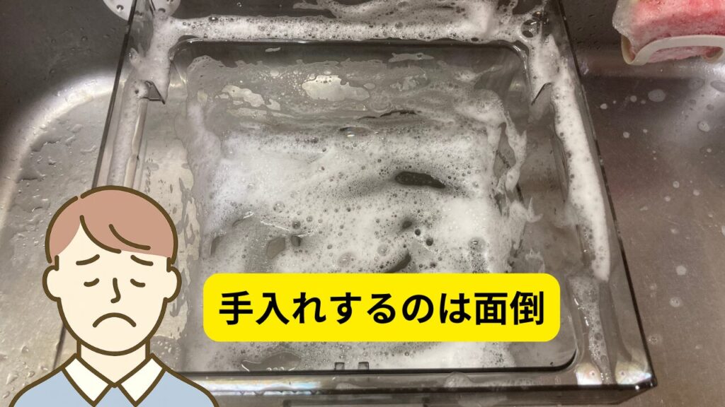 シンクの中で洗剤の泡に覆われた透明な給水タンクと、「手入れするのは面倒」というテキストと共に困った表情を浮かべる男性のイラスト。